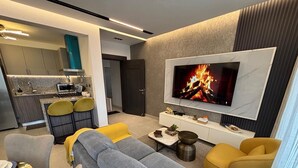 A modern living room with a sofa, yellow chairs, a coffee table, and a TV displaying a fire. - De Lujo (Santiago de los Caballeros)