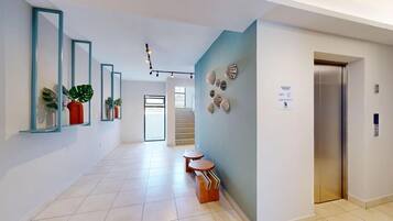 A modern hallway with a staircase, a wall-mounted elevator, and a row of potted plants.