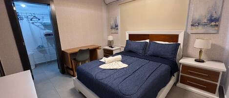 A neatly arranged bedroom with a bed, bedside tables, a desk, and a wardrobe.