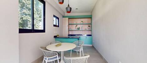 Una cocina moderna con armarios color esmeralda, una mesa de comedor blanca con sillas de mimbre e iluminación colgante.