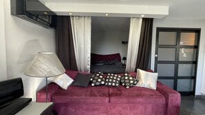 Um quarto com um sofá vermelho, uma luminária, uma TV e uma cama com cortinas.