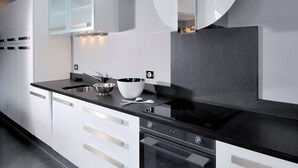 Uma cozinha moderna com armários brancos, bancada preta, fogão e forno embutido.