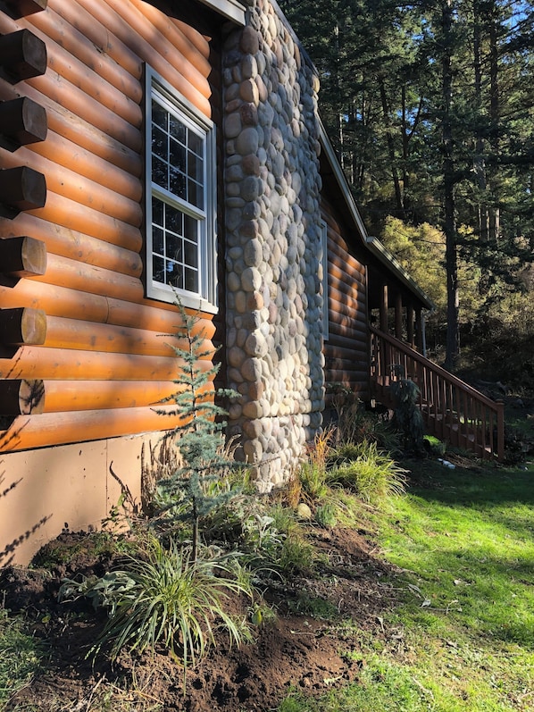 A log cabin with a stone chimney, a wooden deck, and a surrounding forest.