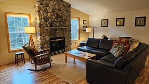 A living room with a stone fireplace, a leather sofa, a rocking chair, and a wooden coffee table.