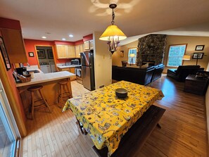 A kitchen with wooden cabinets, a refrigerator, and a dining area with a table covered in a yellow tablecloth.
