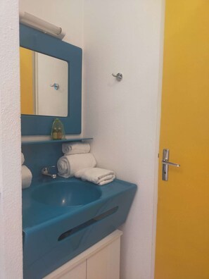 A bathroom with a blue sink, a mirror, a towel rack, and a yellow door. - Port Nature Studio 853 - 2 people (AGDE)