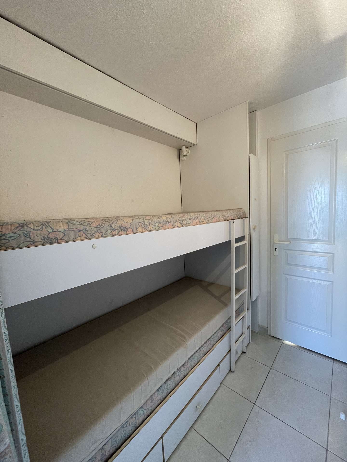 A bunk bed with a ladder, a door, and a tiled floor.