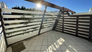 Een betegeld terras met een witte omheining en een houten balk erboven.