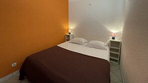 Een kleine kamer met een enkel bed, een bruine sprei, twee bedlampjes en een nachtkastje.