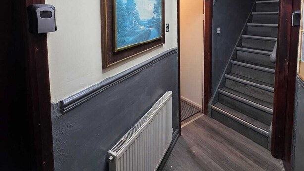 A hallway with a radiator, a framed painting, a staircase, and a door with a sensor. - Room 3 in sheffield (Sheffield)