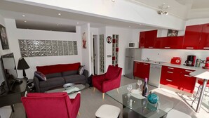 Een moderne woonkamer met een grijze bank, rode fauteuils en een glazen salontafel.