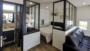 A compact room with a bed, a sofa, a small bathroom, and a window. - VOLUPTIA  - Villa Port Nature 54 - Luxury - 4 people (AGDE)