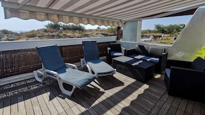 A covered outdoor seating area with lounge chairs and a sofa, overlooking a beach. - VOLUPTIA  - Villa Port Nature 54 - Luxury - 4 people (AGDE)
