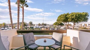 A balcony with a round table and chairs, palm trees, and a view of a cityscape. - CARESSE - Studio Port Nature PN620 - Luxe - 2 people (AGDE)