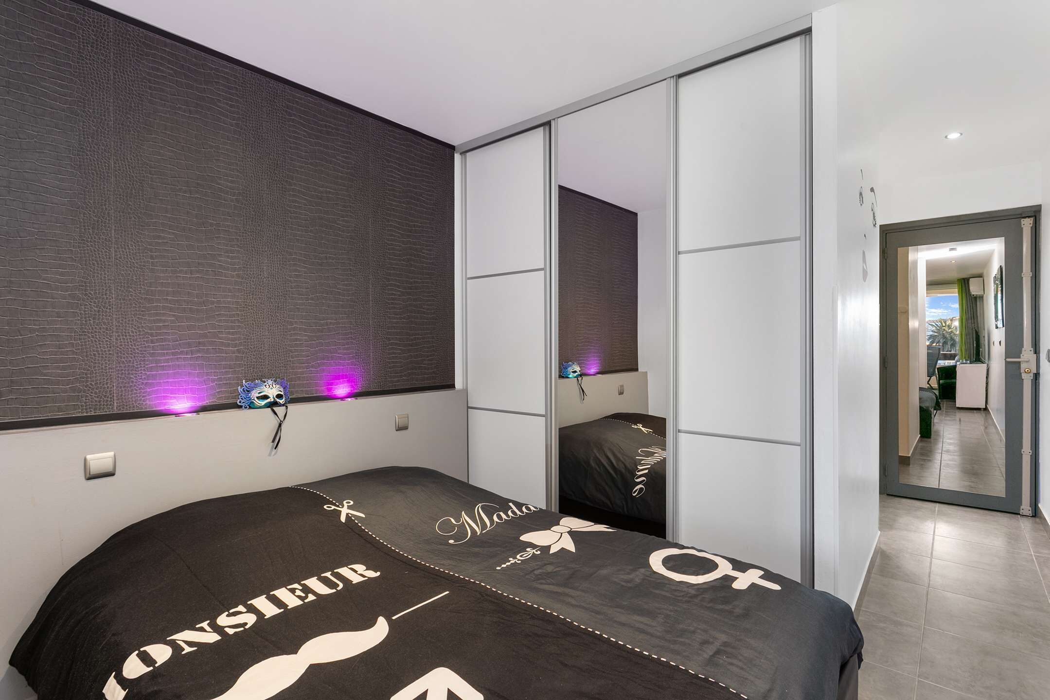A bedroom with a bed, a mirror, and a sliding door leading to a bathroom.