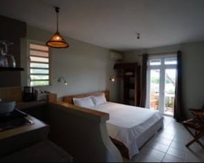 Un dormitorio con cama, escritorio, silla, lámpara colgante y vista al exterior a través de una puerta.