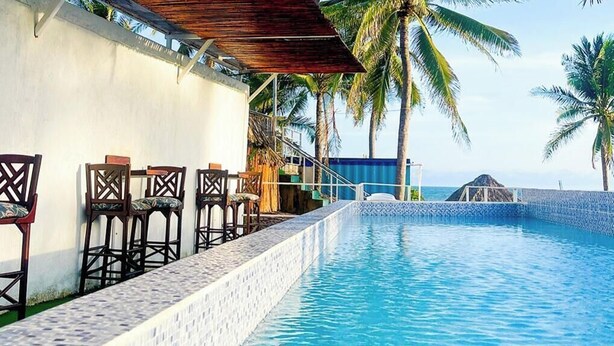 Un espace aménagé au bord de la piscine, avec une structure en bois, des chaises et des palmiers.