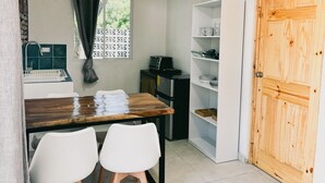 Une petite cuisine avec une table en bois, deux chaises blanches, une étagère blanche et une porte en bois.