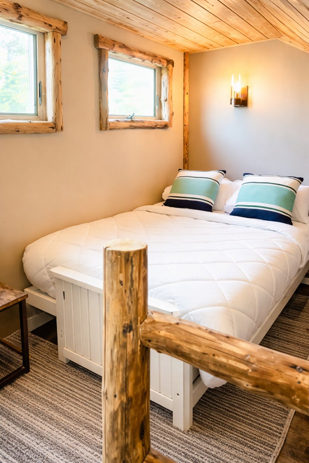 Een slaapkamer met een groot bed, houten hoofdeinde, twee ramen en een wandlamp.