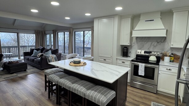 A modern kitchen with a central island, a dining area with a bench, and a living room with a sofa and chairs. - Epic Renovated Slopeside Unit feet from Camelback Mountain- Laurel Glade Trail. (Tannersville)