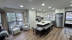 A modern kitchen with white cabinets, a stainless steel refrigerator, and a large window overlooking a deck. - Epic Renovated Slopeside Unit feet from Camelback Mountain- Laurel Glade Trail. (Tannersville)