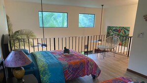 Une chambre à coucher avec un lit, une chaise, une lampe et deux fenêtres.