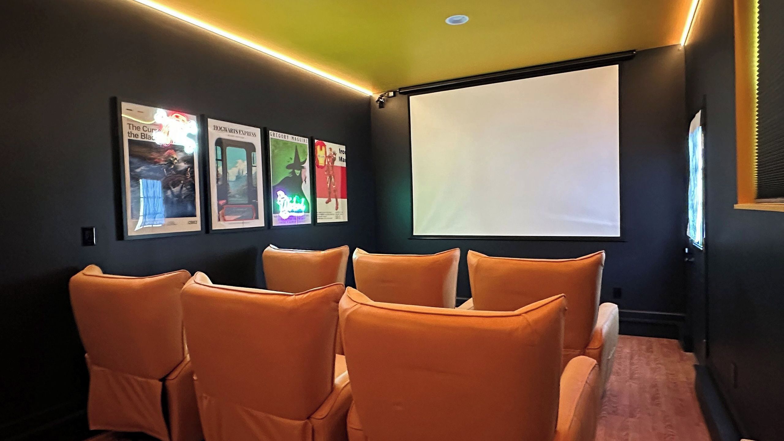 A room with a projector screen, orange chairs, and movie posters on the wall.