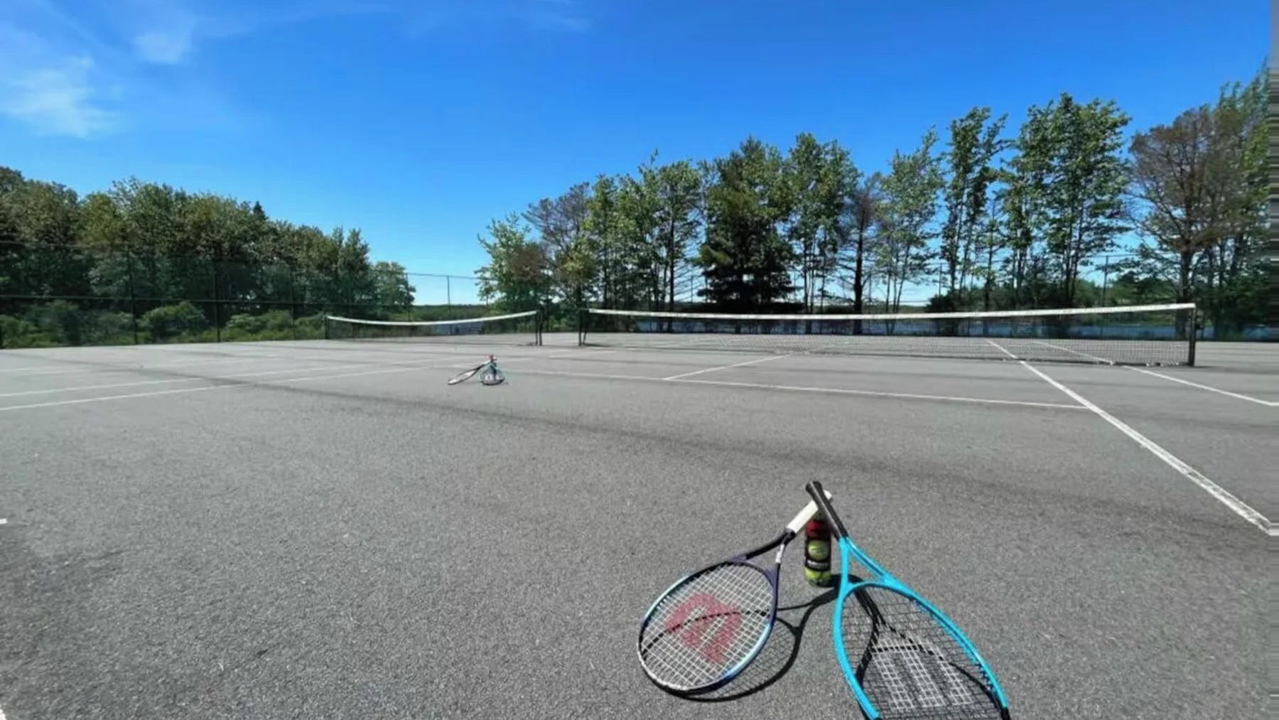 Un campo da tennis all'aperto con una rete, una bicicletta e racchette da tennis.