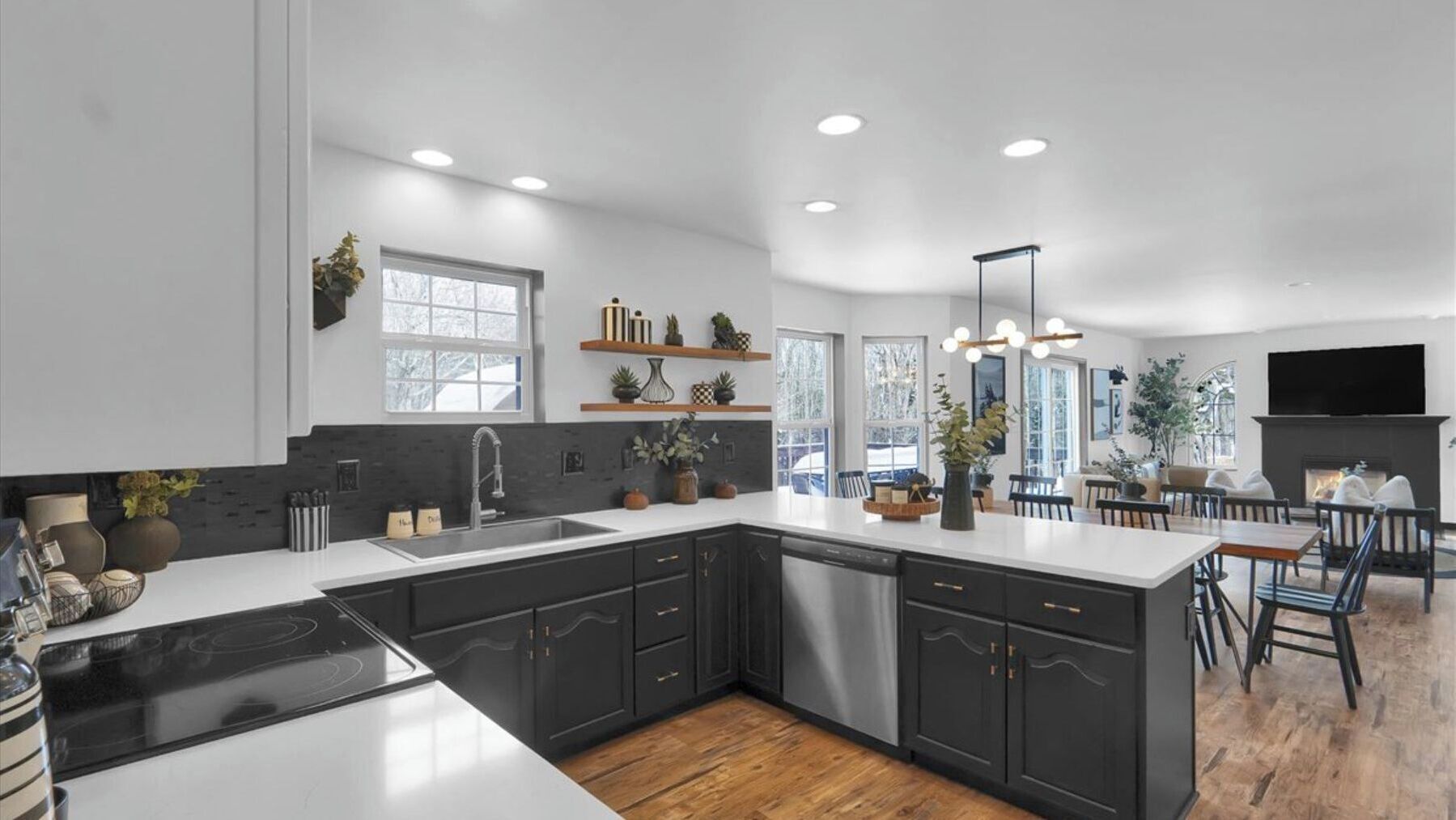 A modern kitchen with dark cabinetry, a central island, and a dining area with a fireplace.