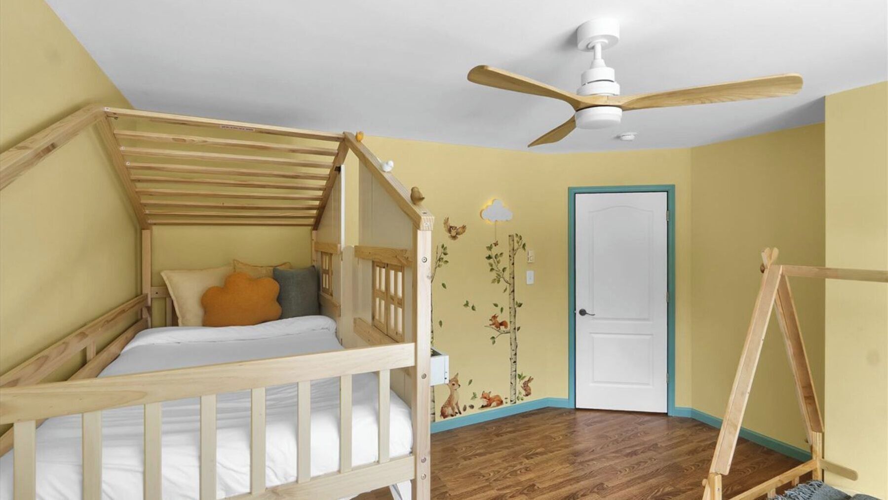 A child's bunk bed with a wooden ladder, a white ceiling fan, and a door with a blue trim.