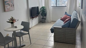 A living room with a sofa, a TV, a table with chairs, a plant, and a painting on the wall. - Beachfront apartment w pools, tennis, gym parking in TOP PR TOURISM CONDADO SJU (Luquillo)