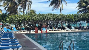 A pool area with blue lounge chairs, a pool, and palm trees. - Beachfront apartment w pools, tennis, gym parking in TOP PR TOURISM CONDADO SJU (Luquillo)