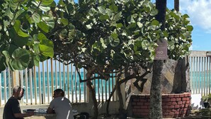 A patio area with a tiled table and benches, a brick wall, and a view of the ocean. - Beachfront apartment w pools, tennis, gym parking in TOP PR TOURISM CONDADO SJU (Luquillo)