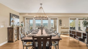 A dining area with a large wooden table, chairs, and a chandelier. There are doors leading to a balcony with a view of the landscape. - El Pomar Estate - Main House by Avantstay Pool + Hot Tub + Firepit + Outdoor Dining + Vineyard Views (Templeton)