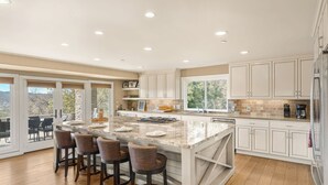 A spacious kitchen with a large island, bar stools, and a view of the outdoors. - El Pomar Estate - Main House by Avantstay Pool + Hot Tub + Firepit + Outdoor Dining + Vineyard Views (Templeton)