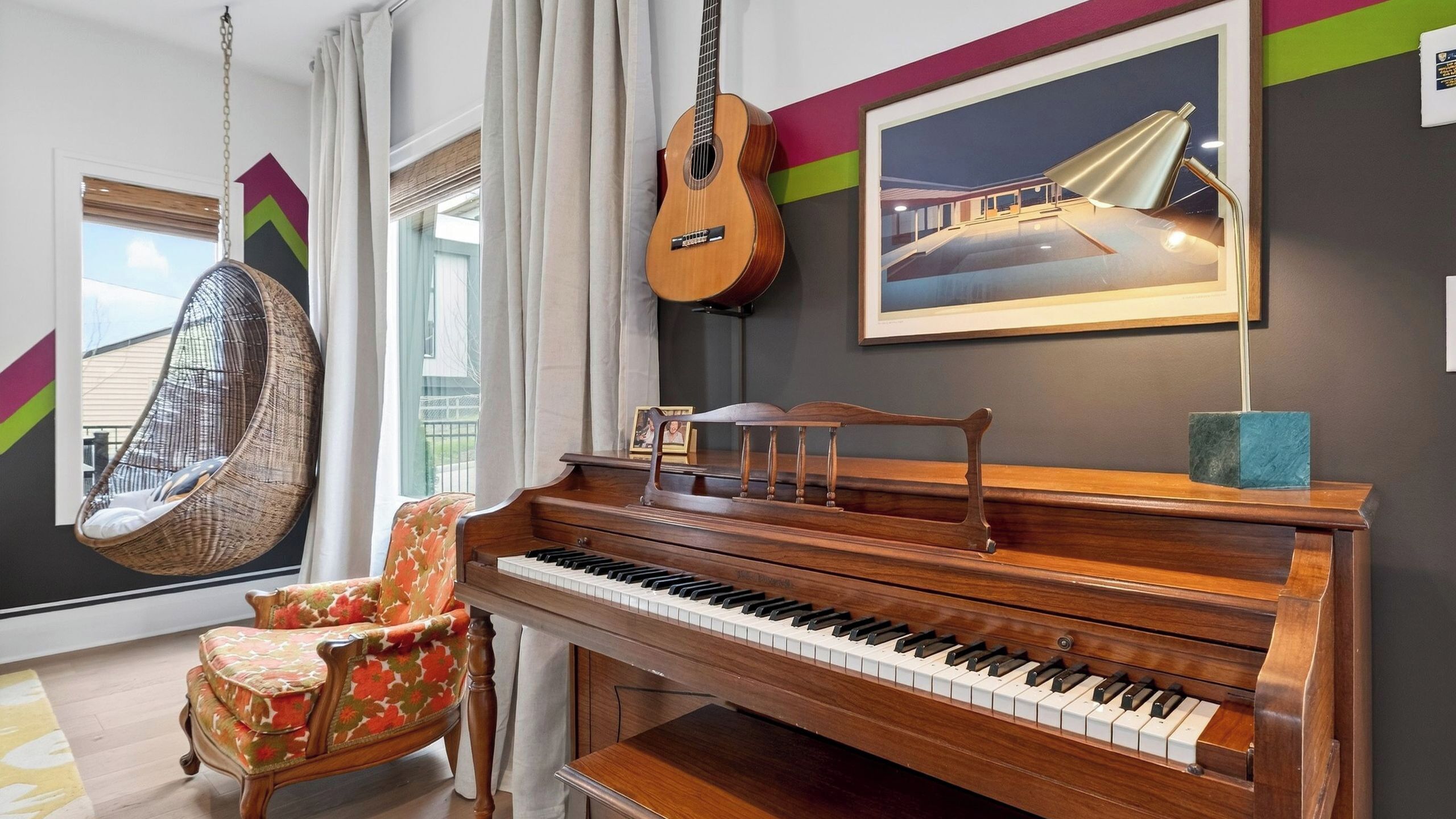 A room with a piano, a guitar, a hanging chair, and a framed picture on the wall.