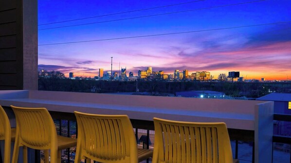 Un balcon avec des chaises jaunes et une vue sur les toits de la ville au crépuscule.