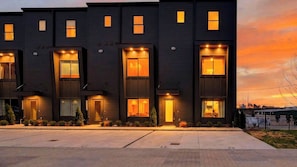 Un immeuble résidentiel moderne à plusieurs étages, doté de fenêtres illuminées et d’une allée bien entretenue.