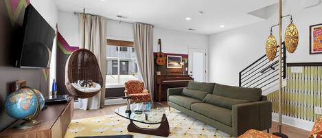 A living room with a sofa, a hanging chair, a glass coffee table, a globe, and a piano.
