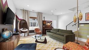 A living room with a sofa, a hanging chair, a glass coffee table, a globe, and a piano. - That 70s Show by Avantstay Skyline Views + Rooftop Hot Tub + Bumper Pool Mins to Broadway + Nissan Stadium + Germantown (Nashville)