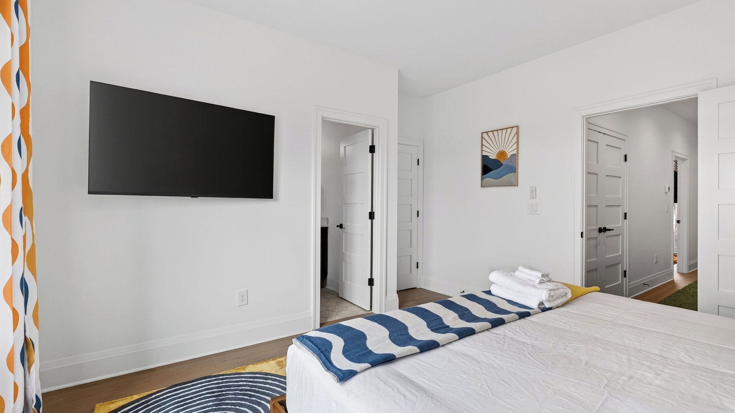 A hotel room with a bed, a television, a painting, and a door leading to another room.
