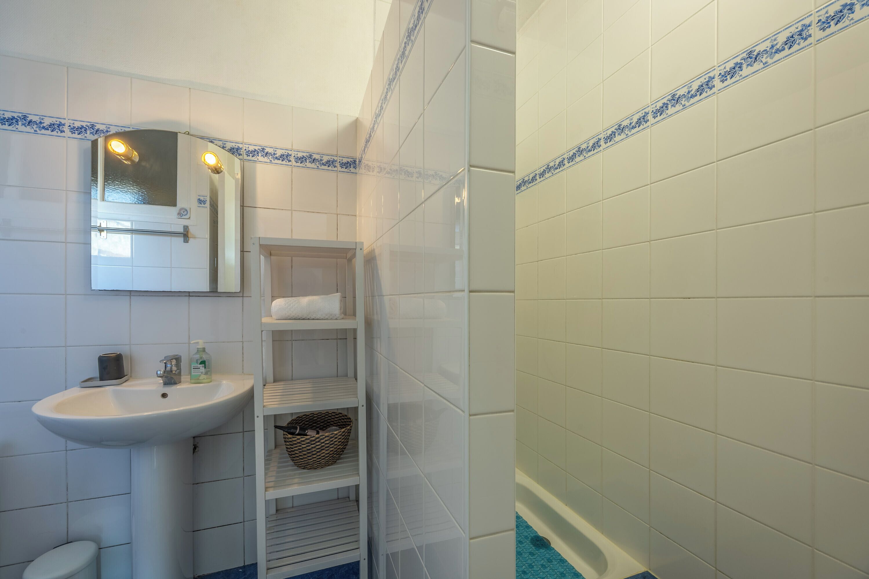 A bathroom with a sink, mirror, shelves, and a shower.