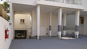 Um edifício com área externa coberta, colunas, extintor de incêndio e entrada com portão.