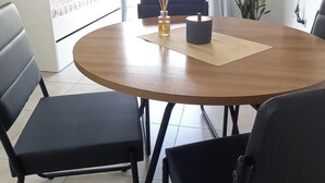Un salon moderne avec une table ronde en bois, des chaises noires, un canapé et un téléviseur fixé au mur.