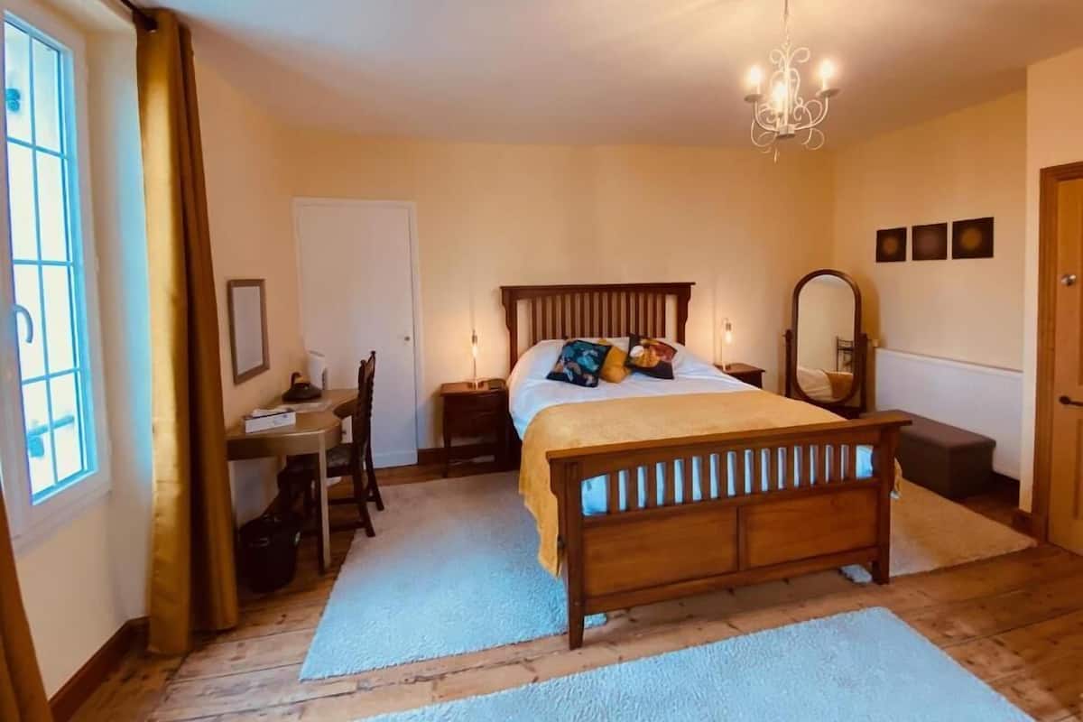 A bedroom with a wooden bed, bedside lamps, a desk, and a chair.