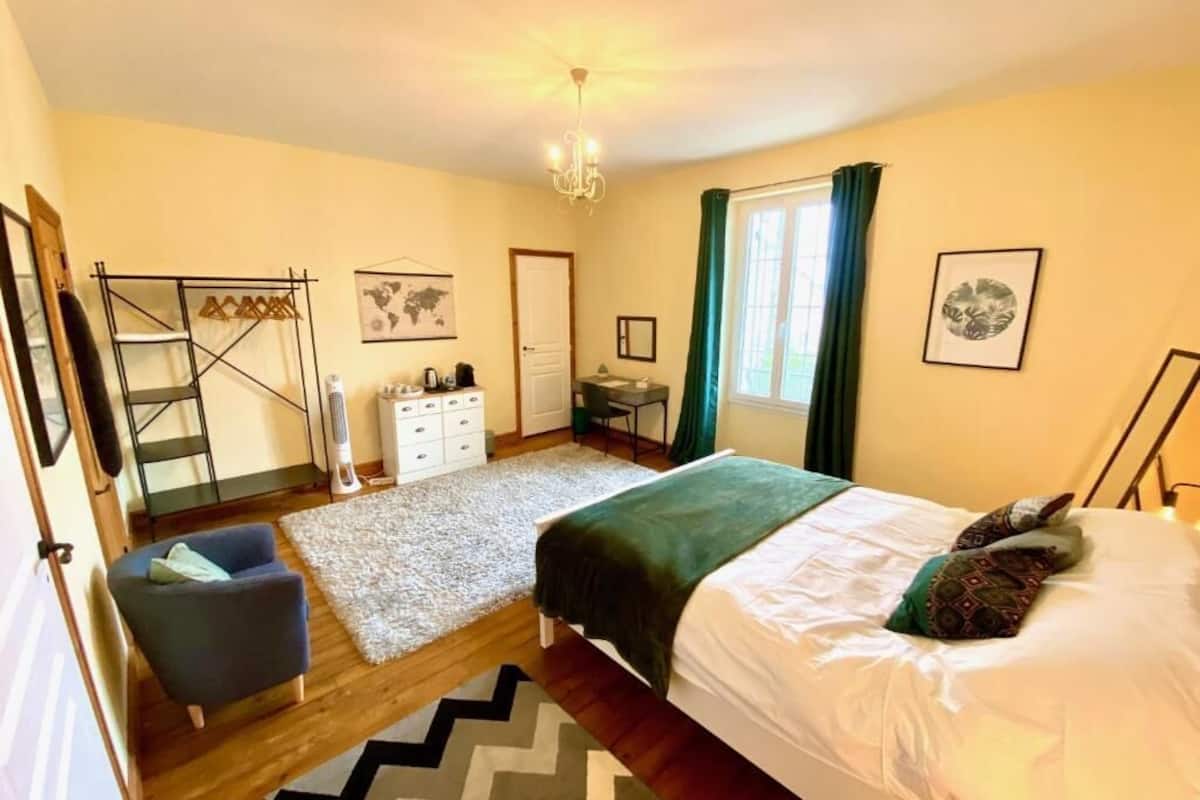 A bedroom with a bed, a desk, a chair, a wardrobe, a hanging rack, a map on the wall, and a window with curtains.