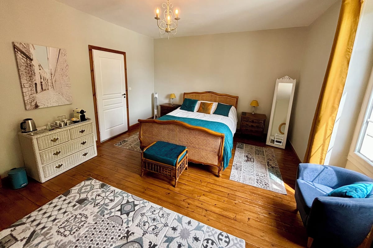 A bedroom with a bed, dresser, chair, and a chandelier.
