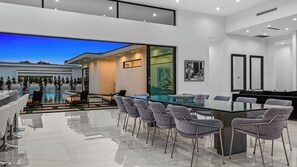 A modern kitchen with a glass island, grey chairs, and a dining area with a glass table. - 2 Luxury Villas Pickleball Court, Pool, Putting Green Bravo by Avantstay (Indio)