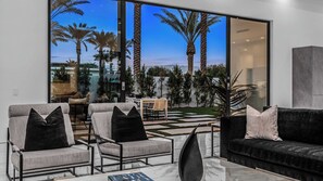 A modern living room with a glass wall, a black sofa, two armchairs, and a coffee table. - 2 Luxury Villas Pickleball Court, Pool, Putting Green Bravo by Avantstay (Indio)