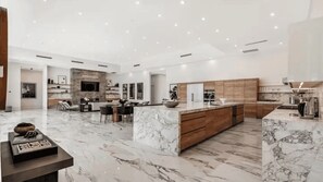 A spacious kitchen with marble countertops, wooden cabinets, and a central island. - 2 Luxury Villas Pickleball Court, Pool, Putting Green Bravo by Avantstay (Indio)